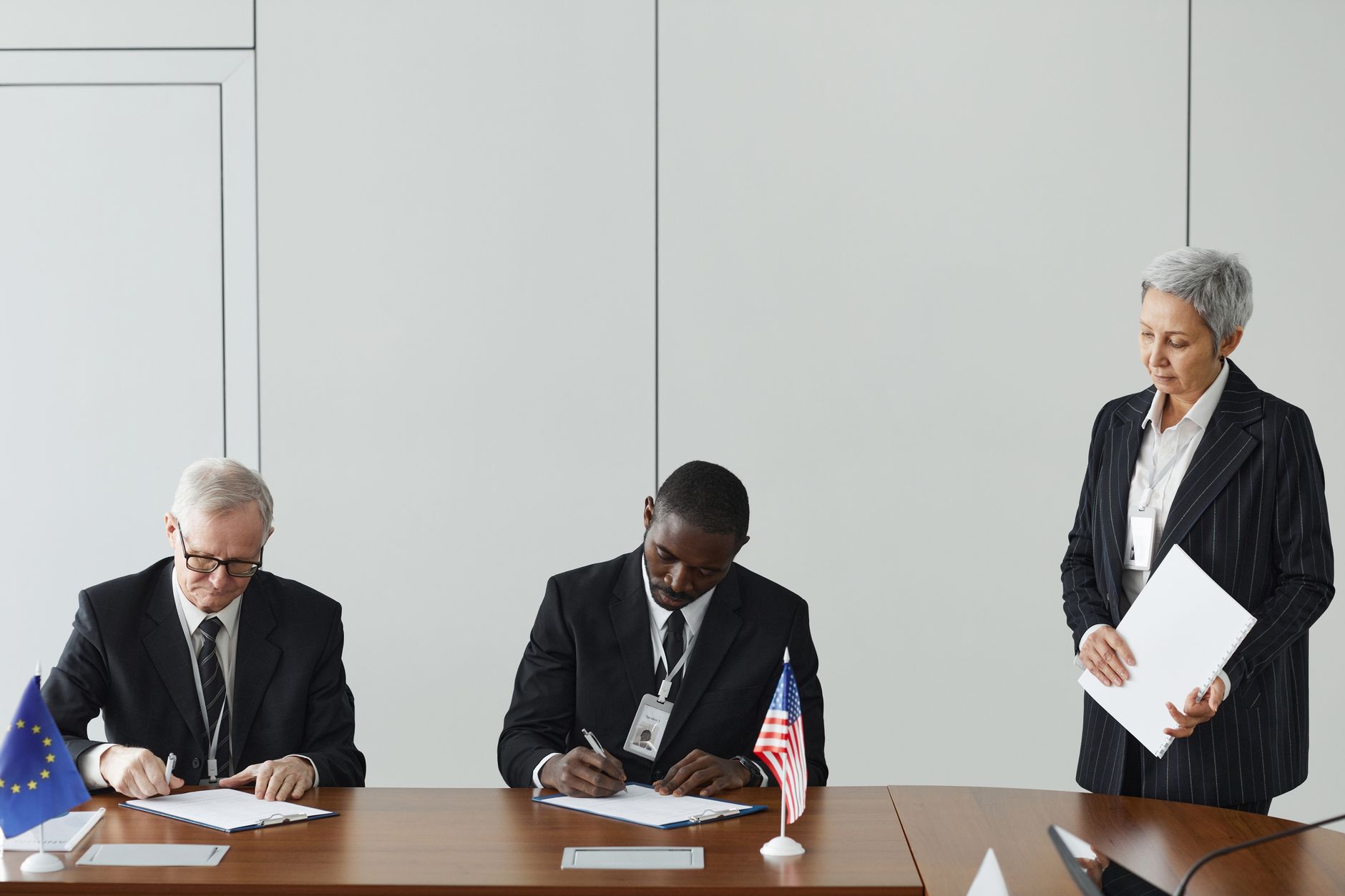 Dyplomaci podpisują dokumenty przy flagach Unii Europejskiej i USA
