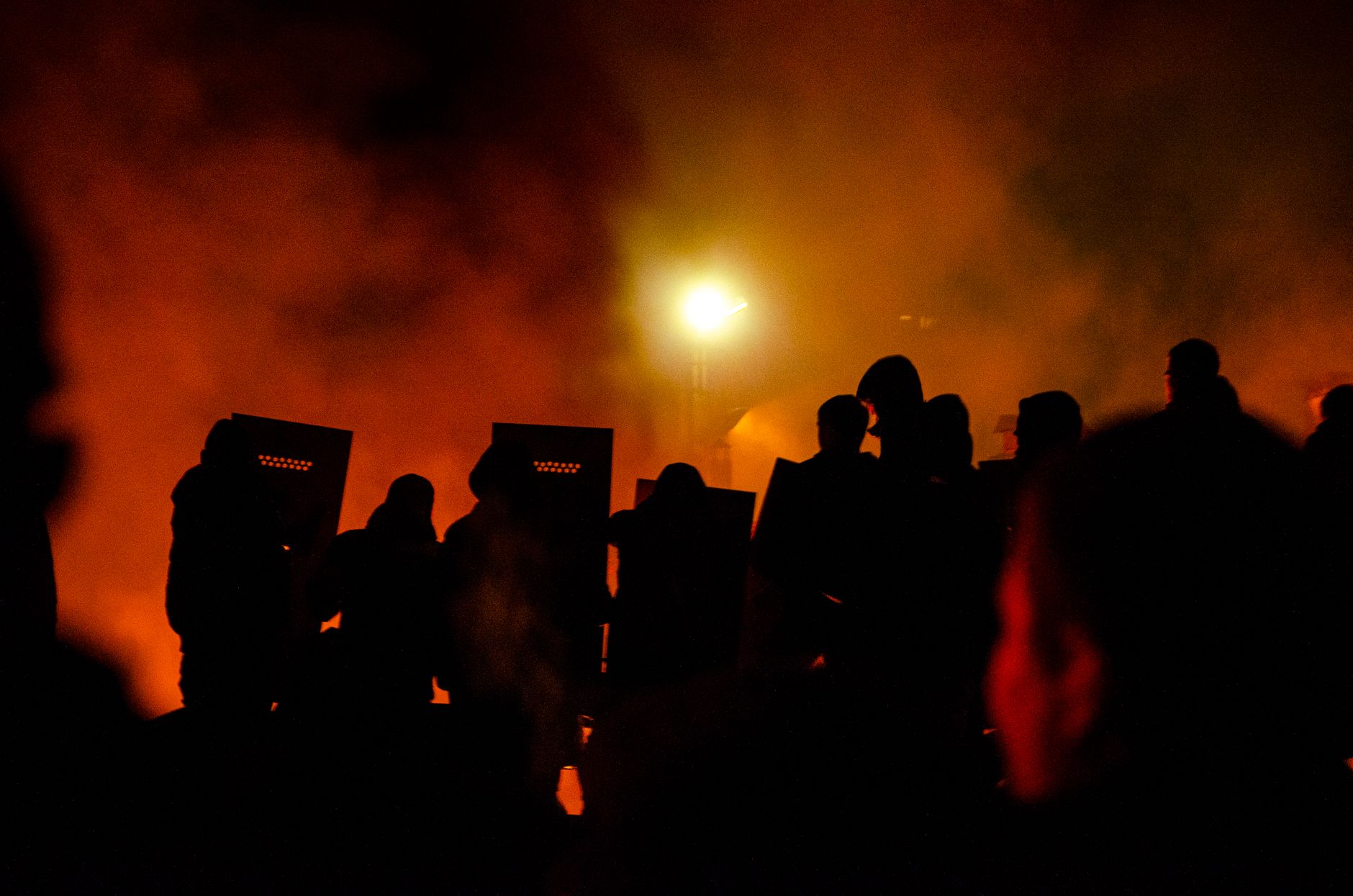 Sylwetki policjantów z tarczami w dymnej nocnej scenerii